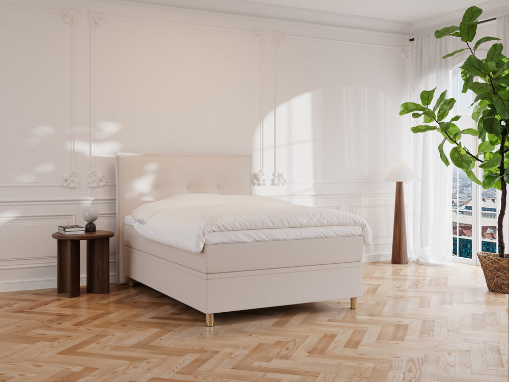 Kontinentalseng Alva 140x200 i sandfarget stoff, oppbygd madrass og hvit dyne i lyst, minimalistisk soverom.