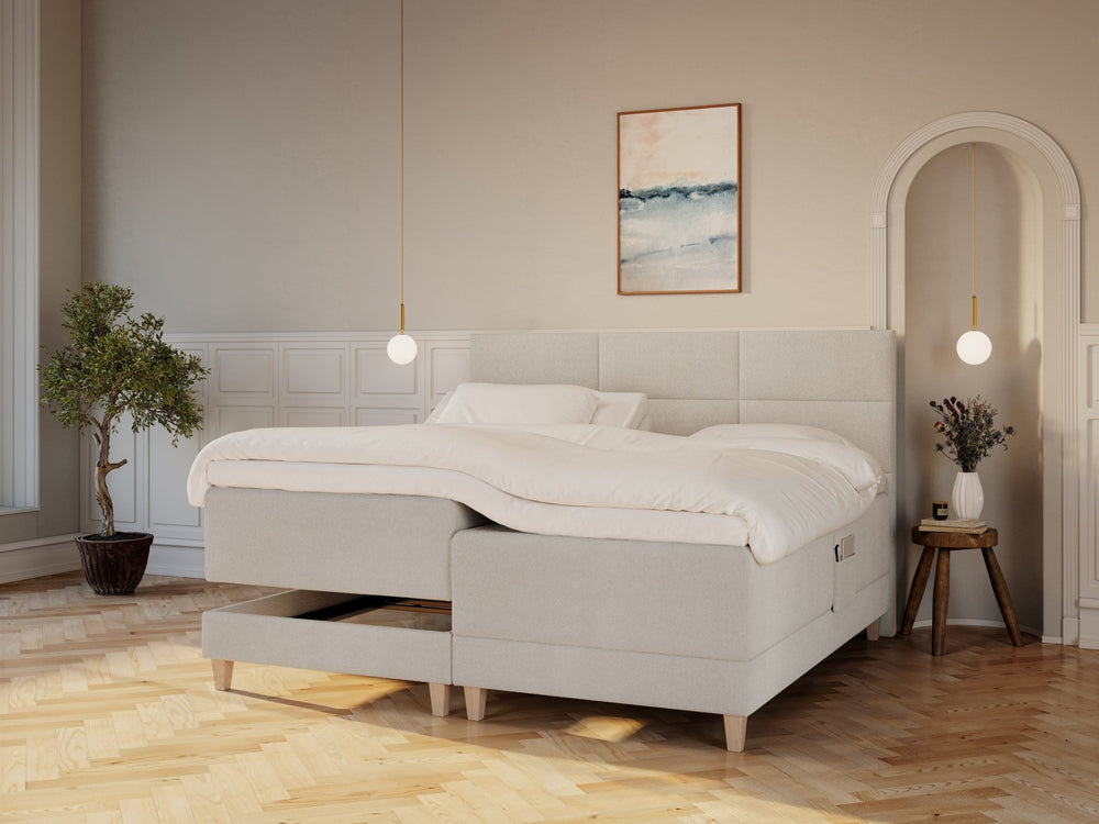 Regulerbar seng i bouclé cream 210x210 med polstret hodegjerde, kremfarget dyne og lys, moderne soveromskomposisjon