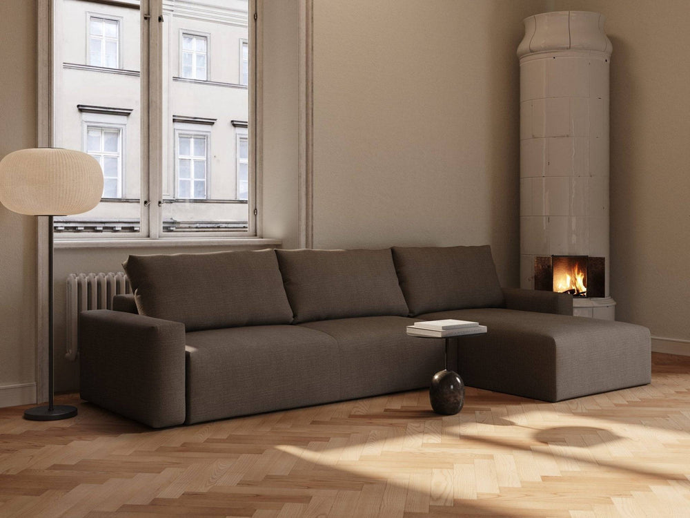 Brun sovesofa Maru 145x342 cm i forest brown, L-formet modul med tekstiltrekk i rom med peis og gulvlampe.