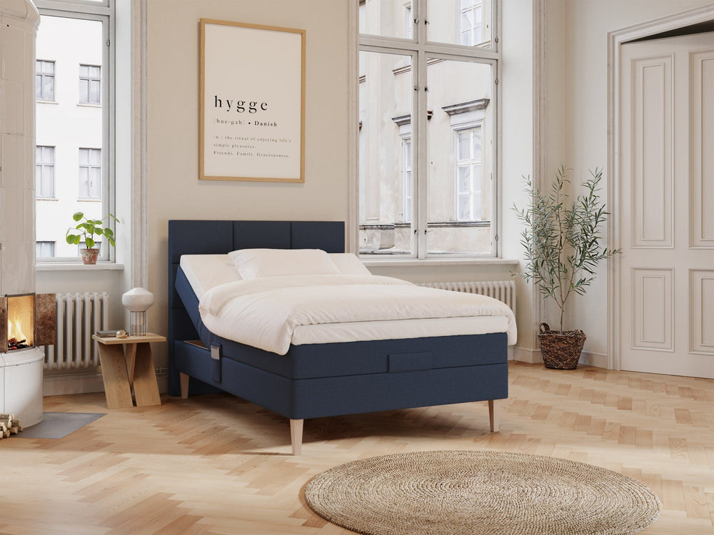 Mørkeblå regulerbar 140x200 seng med hvitt sengetøy i lyst, skandinavisk soverom, stoffhodegjerde og treben.